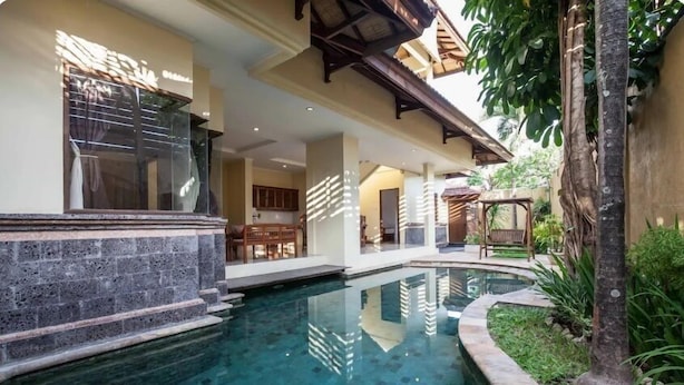 A swimming pool with a stone border, a wooden deck, and a covered outdoor seating area.