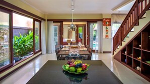 A dining area with a table set for four, a fruit bowl in the center, and a staircase to the right. - Samudra - 1 · 1BR Luxury Private Pool Villa Bali (Kerobokan)