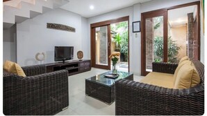 A modern living room with wicker furniture, a flat-screen TV, and a glass coffee table. - SMV - garden - 8-BR · 8BR Garden Villa Walk to Beach and Shops Legian (Legian)