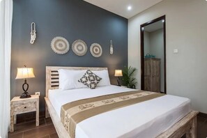 A bedroom with a bed, two bedside tables, a nightstand, a mirror, and wall decorations. - Cecilya Balian Stylish 3 Bedroom House near Beach at City Center (Denpasar)