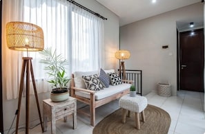 A modern living room with a sofa, two floor lamps, a small table, a potted plant, and a door.