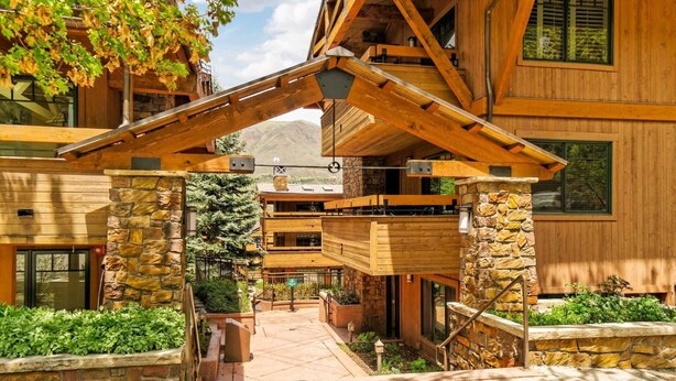 A wooden lodge with a stone entrance, a covered walkway, and a view of the surrounding forest.