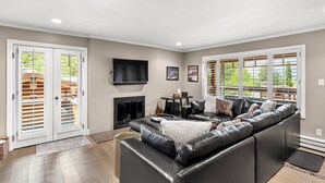 A living room with a leather sofa, a flat-screen TV, a fireplace, and large windows.