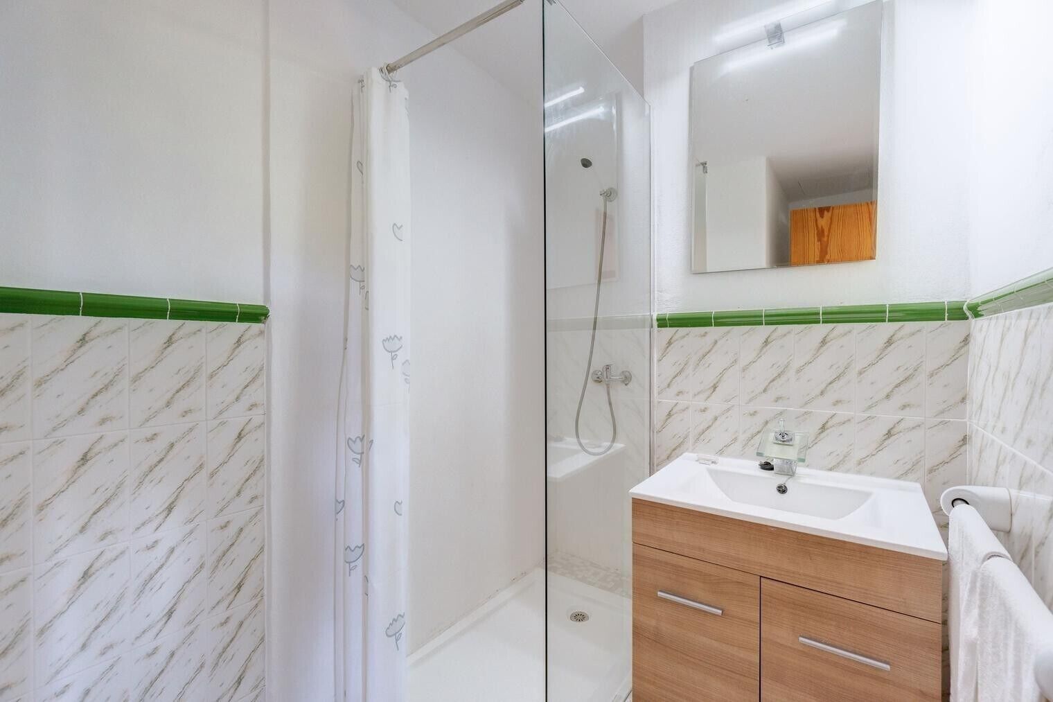 A bathroom with a glass shower enclosure, a sink with a mirror above, and a wooden vanity.