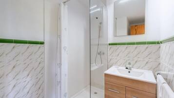 A bathroom with a glass shower enclosure, a sink with a mirror above, and a wooden vanity.