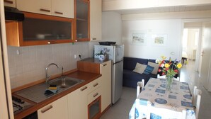 A compact kitchen with a sink, stove, and refrigerator, a dining table with a patterned tablecloth, and a sofa in the adjacent living area.