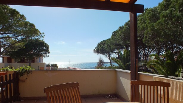 A wooden table and chairs on a balcony with a view of the sea and trees.