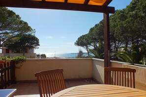 A wooden table and chairs on a balcony with a view of the sea and trees.