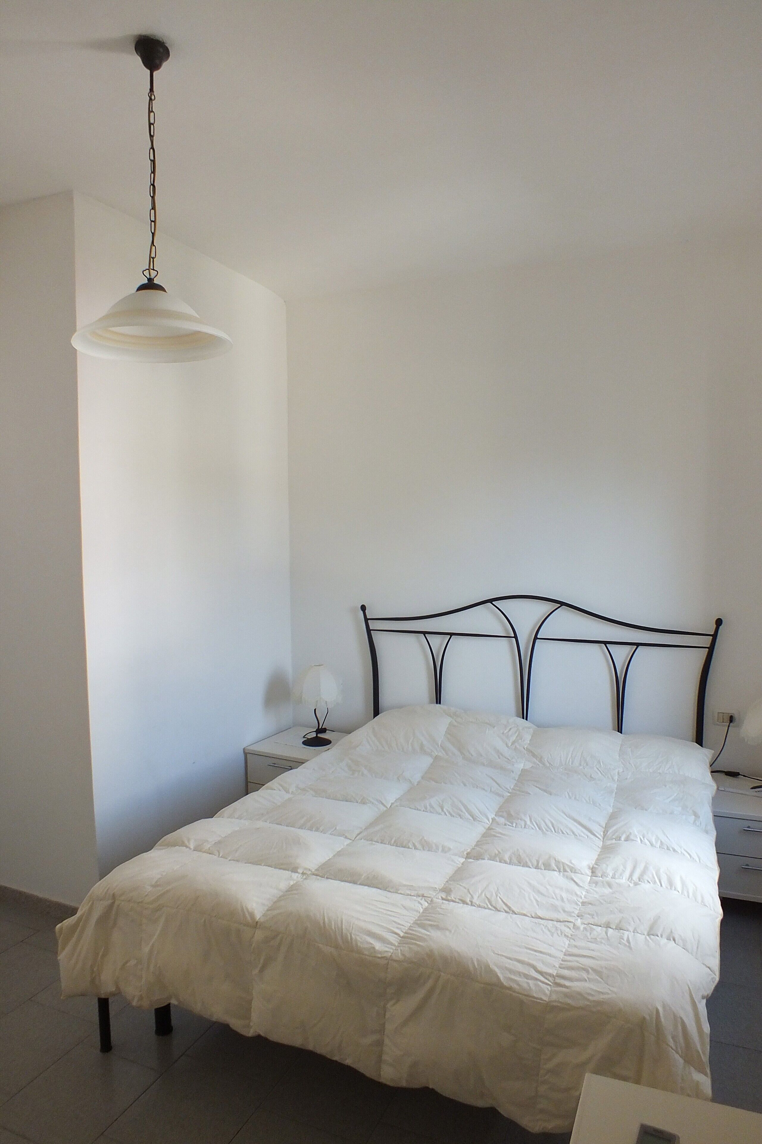 Una camera da letto con un letto, un comodino, una lampada a sospensione e una presa a muro.