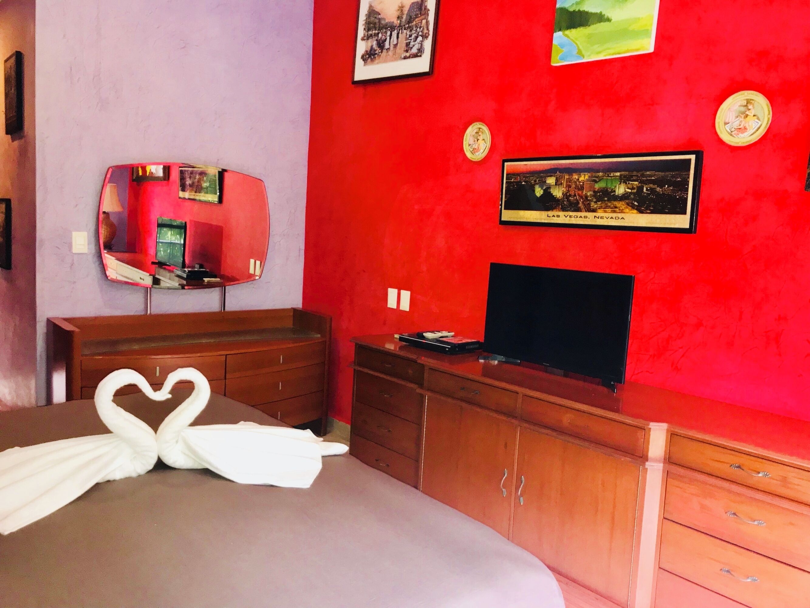 A hotel room with a bed, a dresser, a TV, and wall decorations including a framed picture of Las Vegas.
