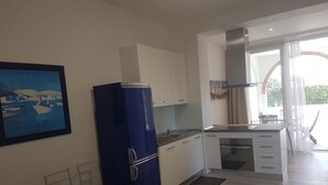 Una cocina moderna con armarios blancos, un refrigerador azul y un comedor con dos taburetes.