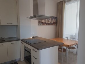 Moderni keittiö, jossa on sisäänrakennettu liesi, ruokapöytä tuoleineen ja ikkunasta avautuva näkymä ulos.