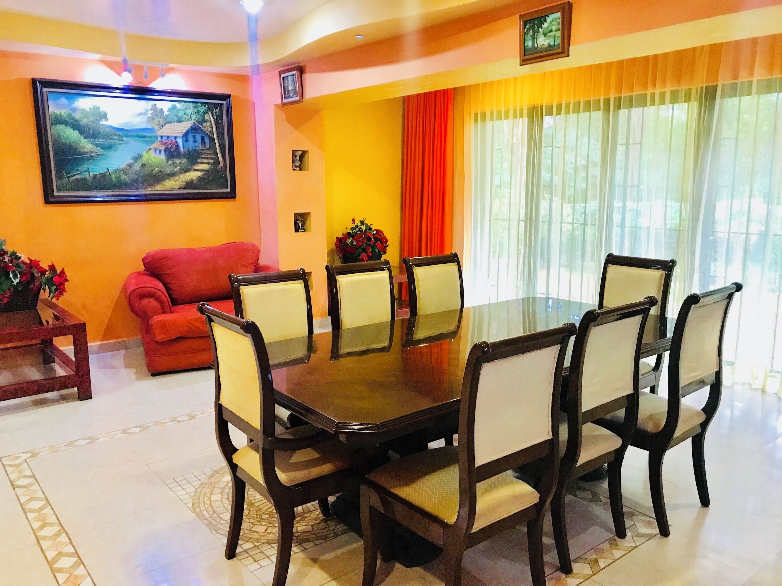 A dining area with a round table and six chairs, a red sofa, and a painting on the wall.