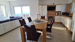 Een moderne keuken met een houten tafel en stoelen, een inbouwoven en een televisie boven de aanrecht.