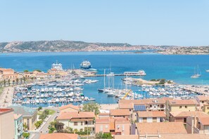 A marina with boats, a large ship, and buildings with red-tiled roofs.