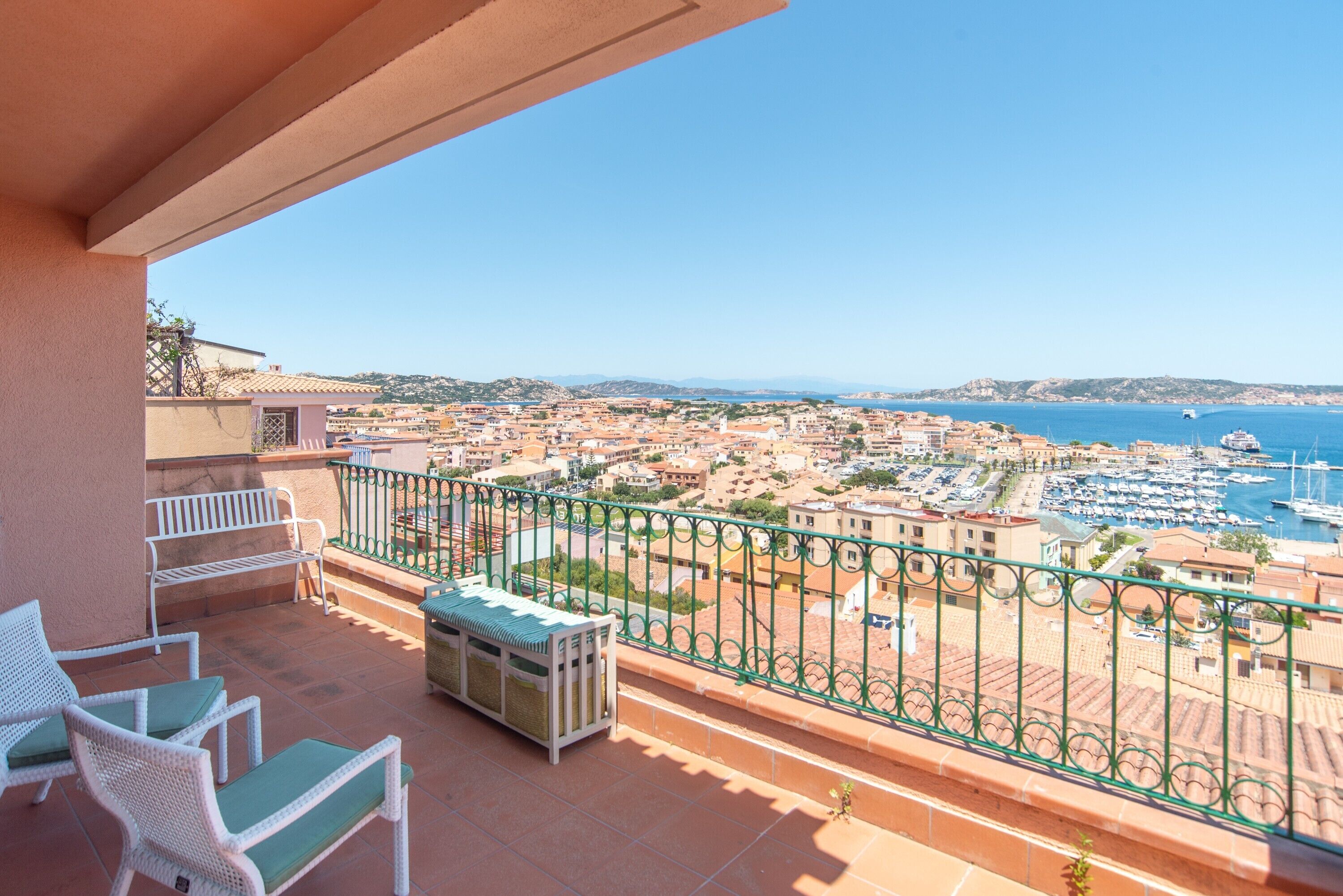 A balcony with outdoor furniture, a view of a marina, and buildings in the distance.