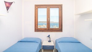 A bedroom with two beds, a window with a view of the sea, and a small desk with a lamp. - Apartment with Panoramic Sea View and Terrace; Pets Allowed (Palau)
