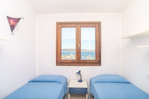Un dormitorio con dos camas, una ventana con vista al mar y un escritorio pequeño con lámpara.