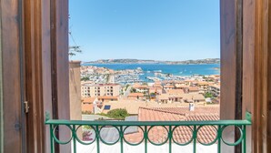 A balcony with a view of a coastal town, buildings, and a marina. - Apartment with Panoramic Sea View and Terrace; Pets Allowed (Palau)