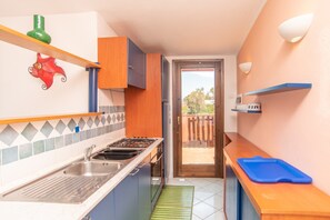 Cocina compacta con pileta, estufa y alacenas, que da a un balcón con baranda de madera.