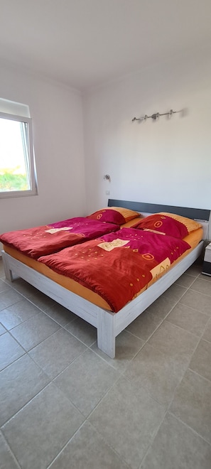 A bed with a white frame and a red and orange bedspread.