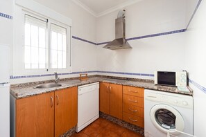 Una cocina compacta con lavavajillas, lavadora, microondas y un ventanal con persianas.
