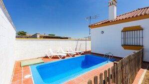 A swimming pool with a wooden fence, a white wall, and a tiled roof.