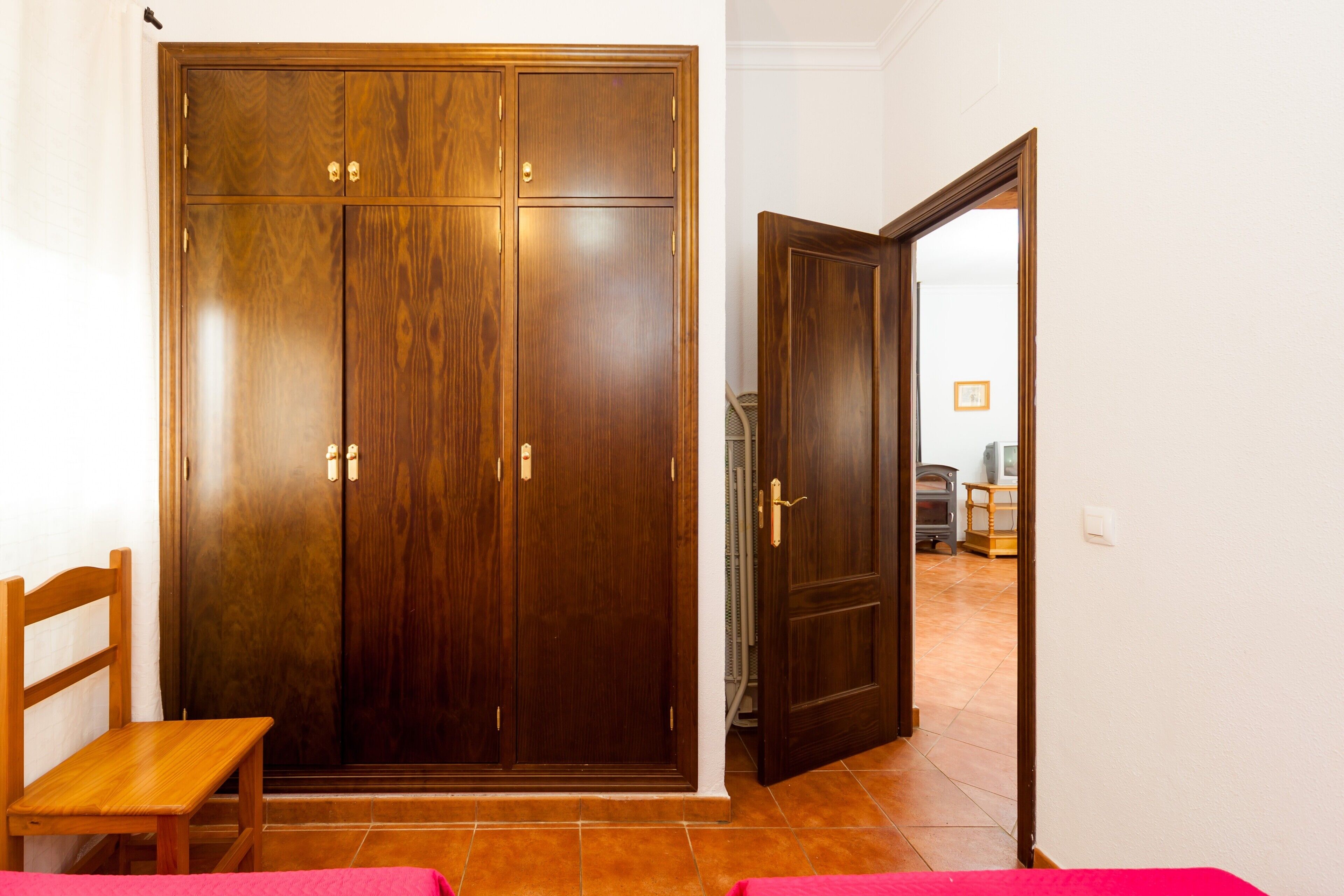 A room with a wooden wardrobe, a bench, and a door leading to another room.