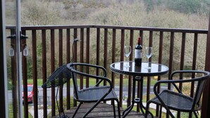 A balcony with a table and two chairs, overlooking a forested area. - Oakridge, St Mellion, Cornwall + 2 Leisure Passes (Saltash)