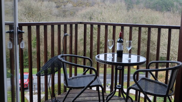 A balcony with a table and two chairs, overlooking a forested area. - Oakridge, St Mellion, Cornwall + 2 Leisure Passes (Saltash)