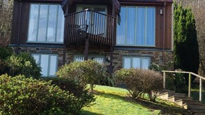 A two-story house with a stone facade, large windows, and a wooden balcony. - Oakridge, St Mellion, Cornwall + 2 Leisure Passes (Saltash)