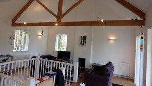 A spacious living room with high ceilings and exposed wooden beams, a comfortable seating area, a fireplace, and a television. - Oakridge, St Mellion, Cornwall + 2 Leisure Passes (Saltash)