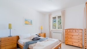 Et soveværelse med en træseng, to sengeborde, en kommode, et vindue med gardiner og et billede på væggen.