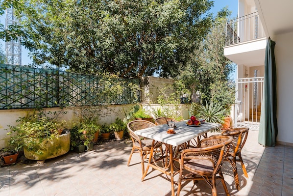 A patio with a table and chairs, surrounded by potted plants and a large tree. - With Terrace, in the Heart of Otranto – Apartment Laura (Otranto)