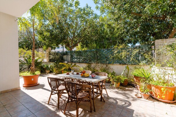 Terrassa a l'aire lliure amb taula i cadires, envoltada de plantes en testos i arbres.