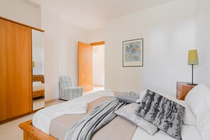 A bedroom with a bed, a wooden wardrobe, a chair, a bedside table, and a lamp.