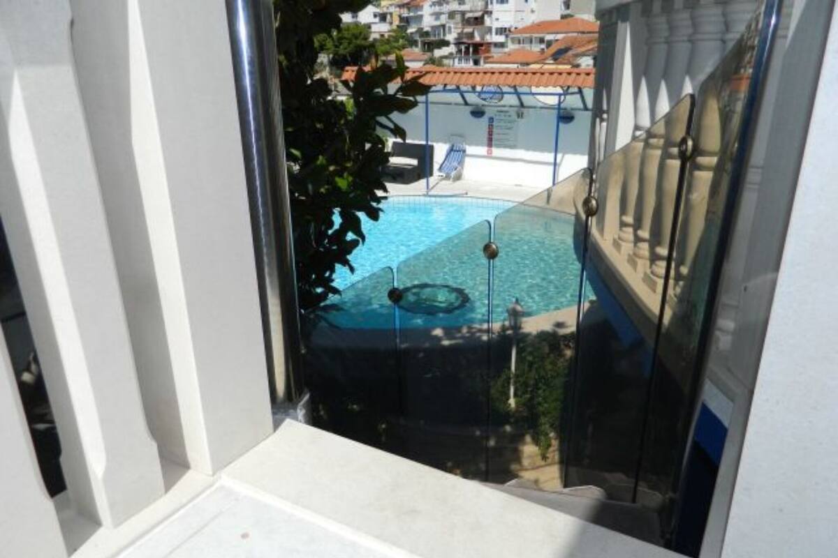 A pool area with a clear view of the pool, a lounge chair, and a building in the background.