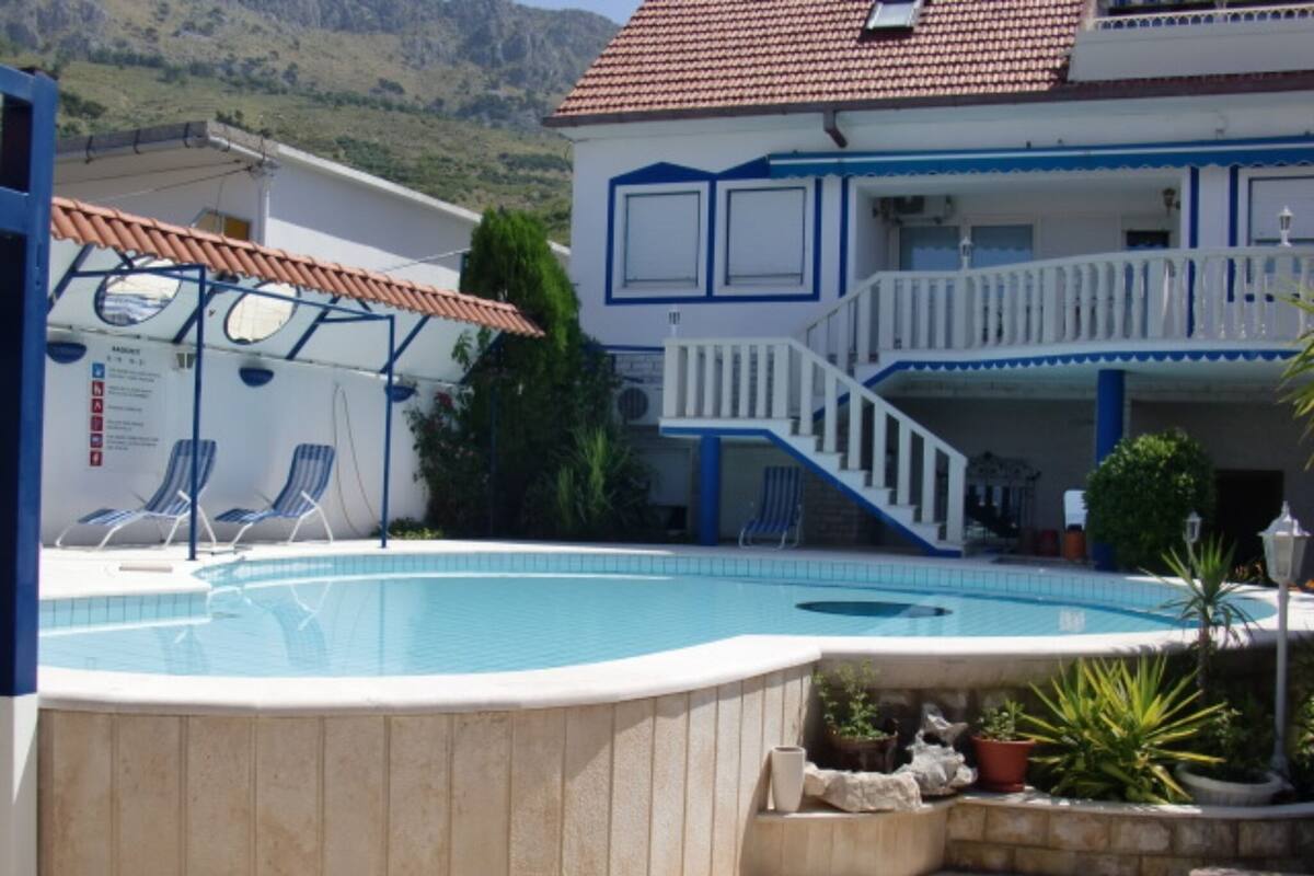 A swimming pool with lounge chairs, a staircase leading to a balcony, and a mountainous backdrop.