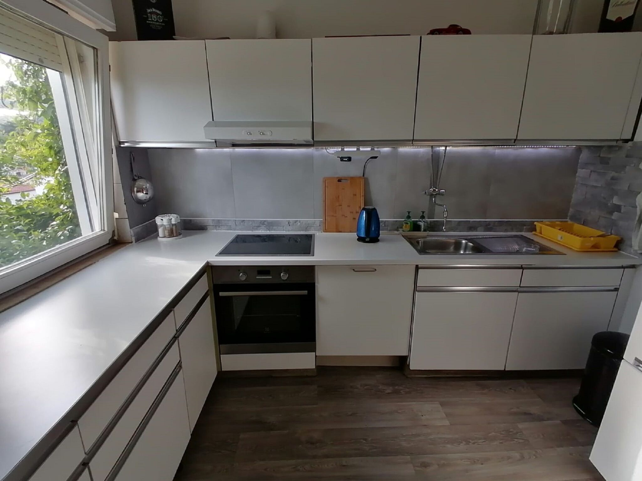 A compact kitchen with white cabinets, a built-in oven, a sink, and a window providing natural light.