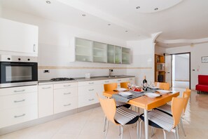 Una cucina moderna con mobili bianchi, forno integrato e zona pranzo con tavolo apparecchiato per quattro persone.