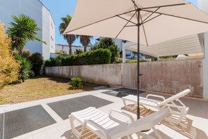 Patio con poltrone bianche, un ombrellone grande, un muro in cemento e piante.
