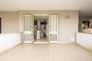 An open balcony with a tiled floor, a dining area with chairs and a table, and a door leading to another room.