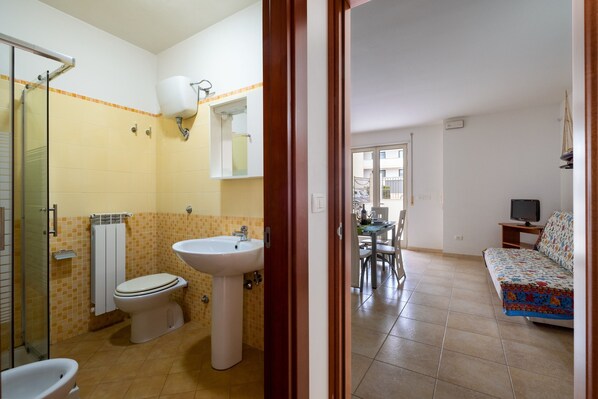 A bathroom with a toilet, sink, and shower, and a living area with a sofa and TV.