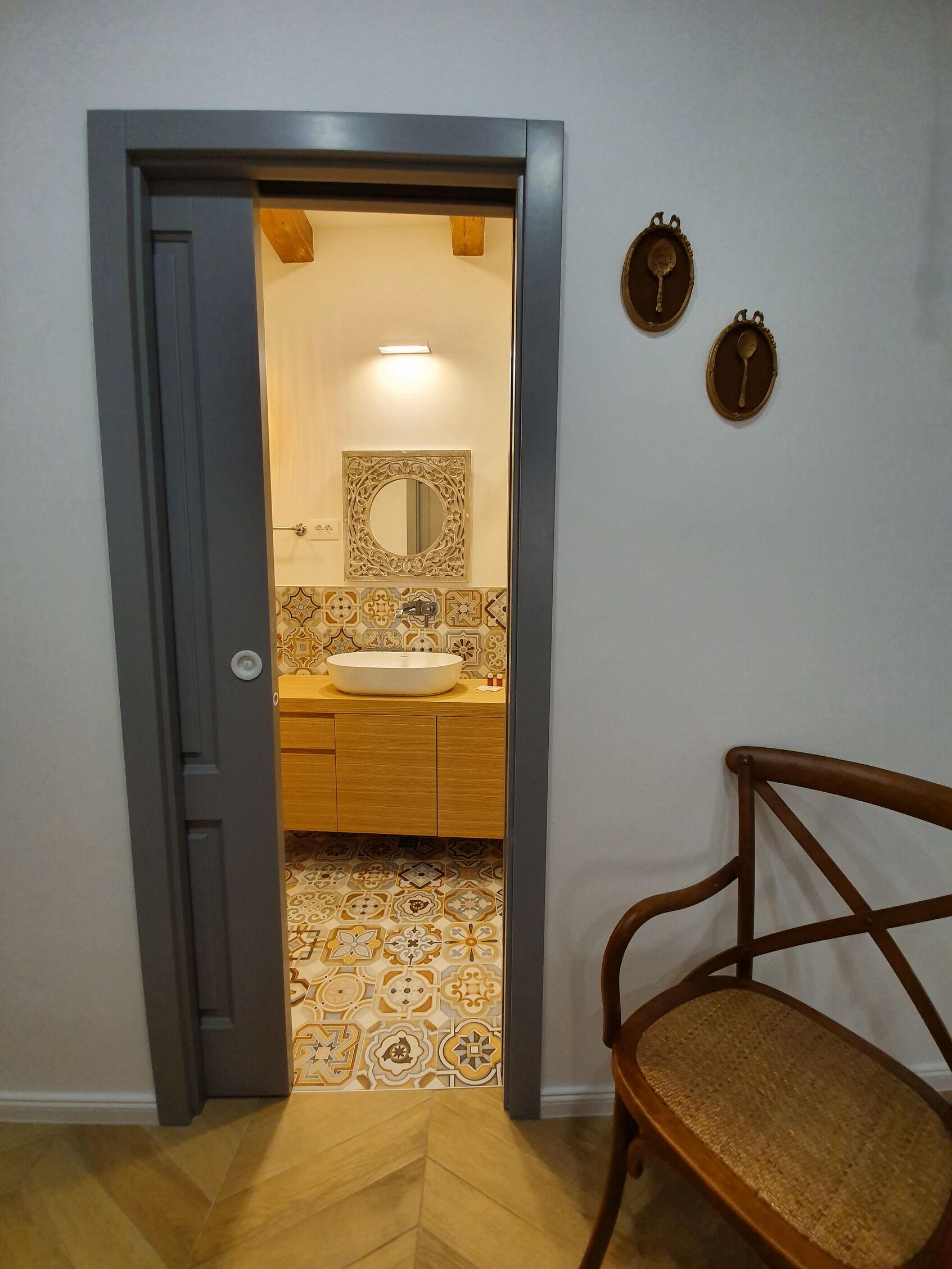 Une salle de bain avec un meuble-lavabo en bois, un lavabo blanc et des carreaux à motifs.