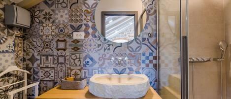 A bathroom with a stone sink, a mirror, and a shower.