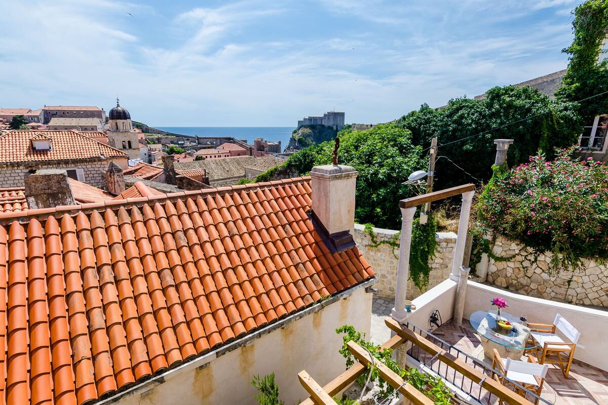 Una terrassa al terrat amb teules de terracota, una paret de pedra i una taula de vidre amb caires.