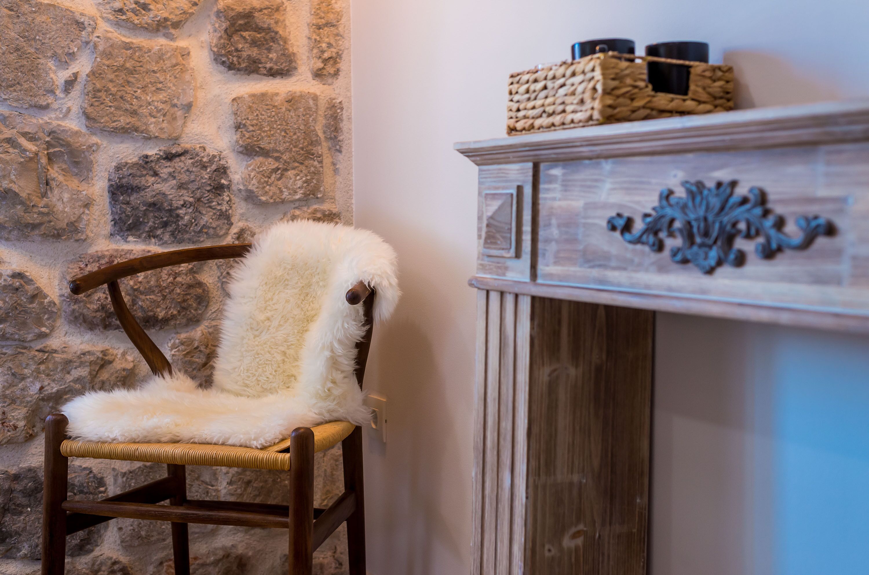 A rustic stone wall, a wooden chair with a fluffy white cushion, and a wooden cabinet with decorative carvings.