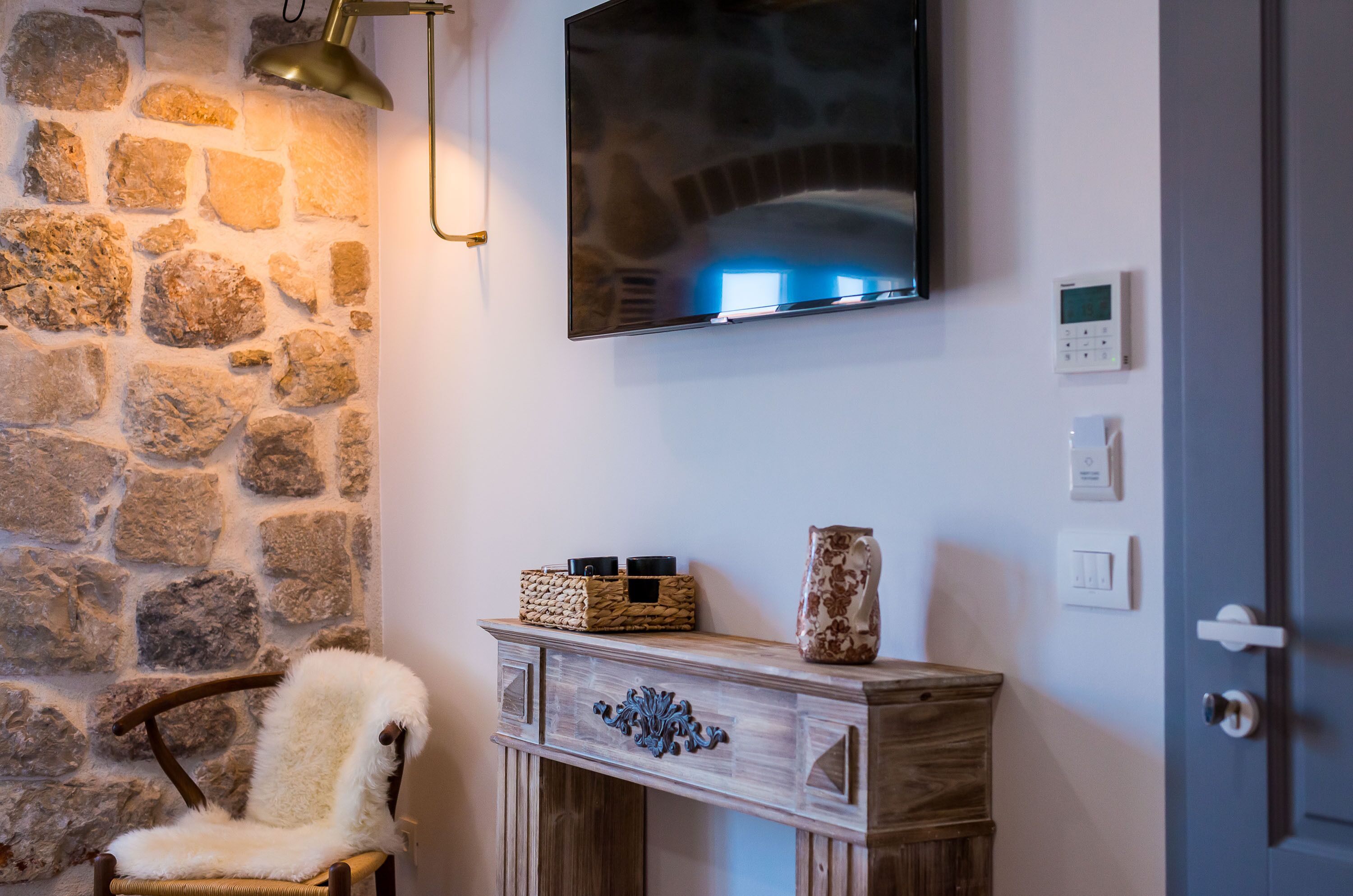 A stone wall, a mounted TV, a wooden console table with decorative items, and a door with a lock.