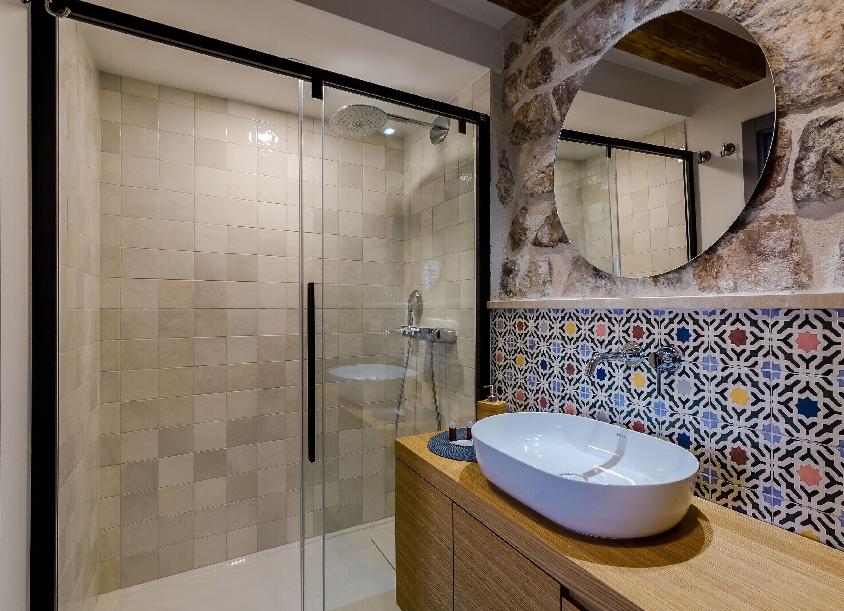 Casa de banho moderna com chuveiro envidraçado, lavatório branco e espelho decorativo com arco de pedra.