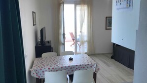 Un comedor con una mesa y sillas, un televisor sobre un mueble bajo, una puerta que da al exterior y una pared con un cartel.